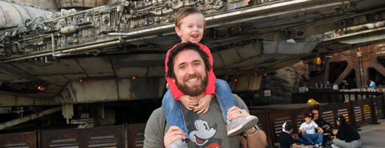 employee chad smiling with son at disney world in front of millenium falcon